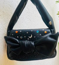 Hand painted galaxy themed black bow handbag photographed outdoors
